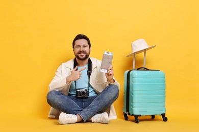 Photo of Traveller with vintage camera, passport, ticket and suitcase on orange background