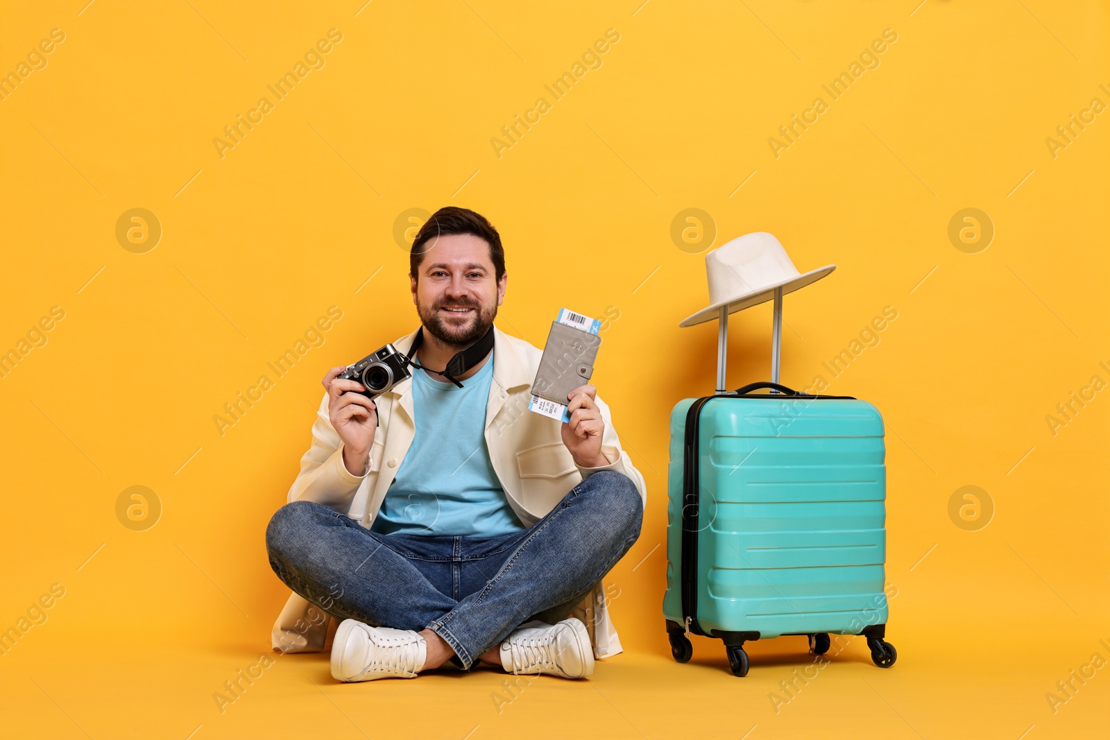 Photo of Traveller with vintage camera, passport, ticket and suitcase on orange background