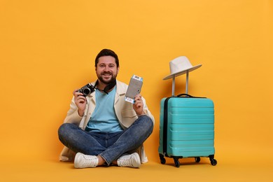 Photo of Traveller with vintage camera, passport, ticket and suitcase on orange background