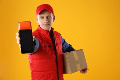 Happy courier with payment terminal and parcel on yellow background