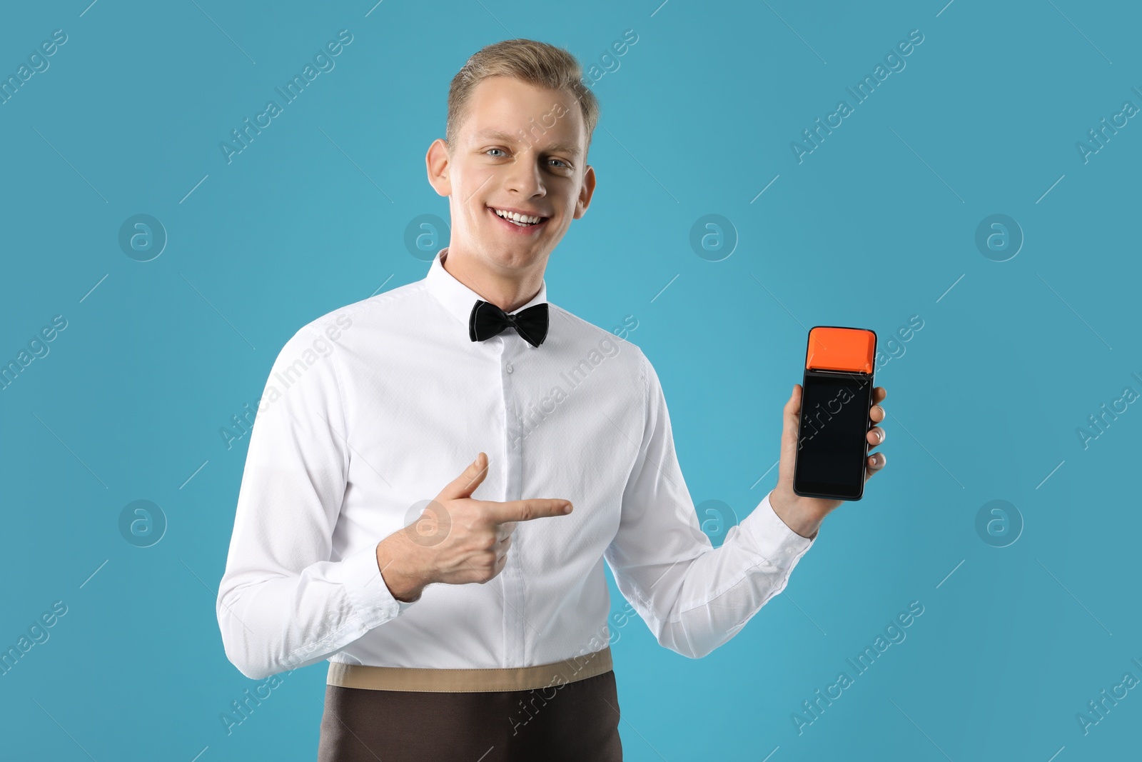 Photo of Happy waiter with payment terminal on light blue background