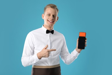 Happy waiter with payment terminal on light blue background