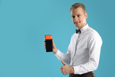 Photo of Happy waiter with payment terminal showing thumbs up on light blue background, space for text