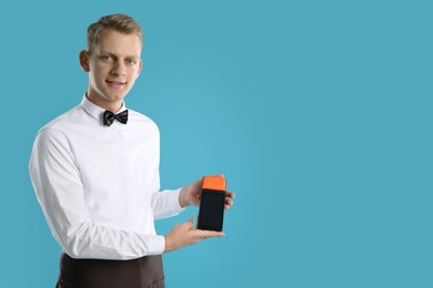 Photo of Happy waiter with payment terminal on light blue background, space for text