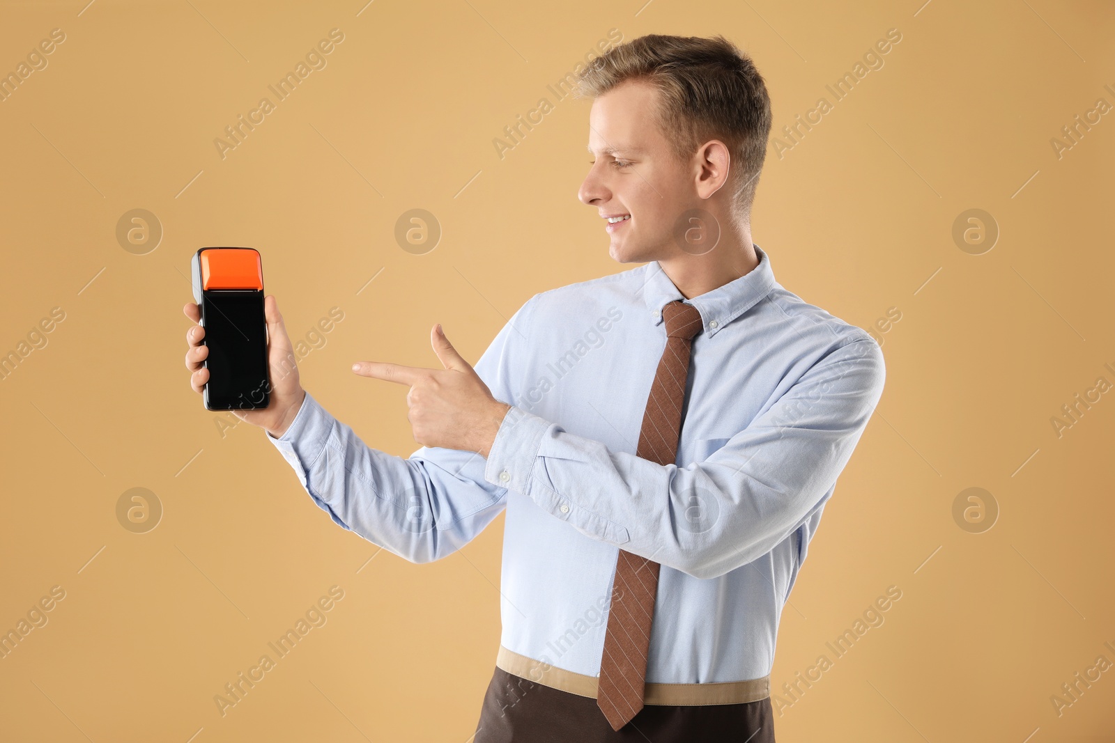 Photo of Happy young man with payment terminal on beige background