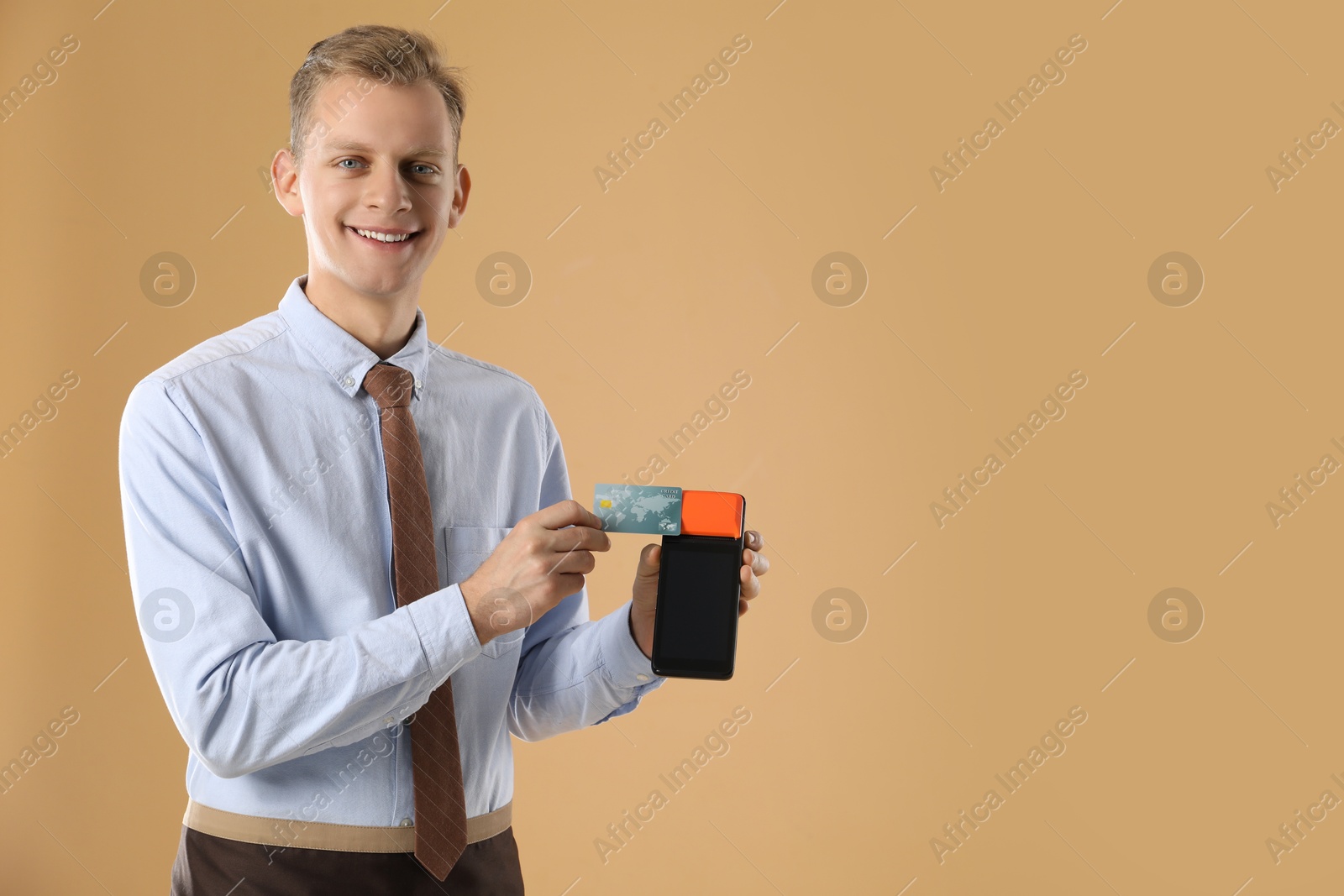 Photo of Happy young man with payment terminal on beige background, space for text