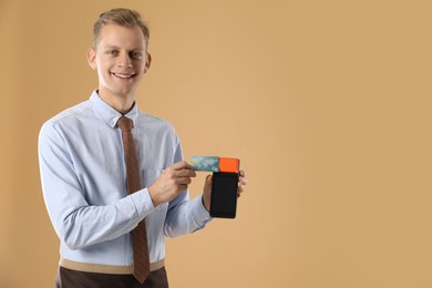 Happy young man with payment terminal on beige background, space for text