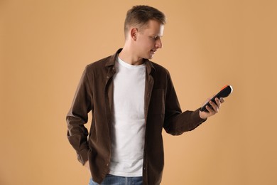 Happy young man with payment terminal on beige background