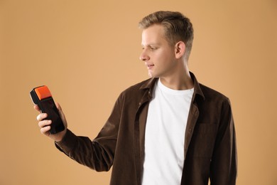 Happy young man with payment terminal on beige background