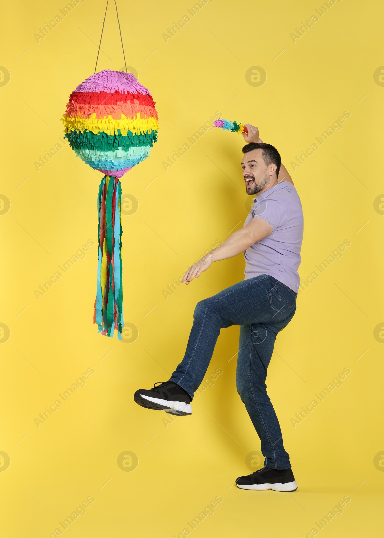 Photo of Emotional man hitting colorful pinata with stick on yellow background