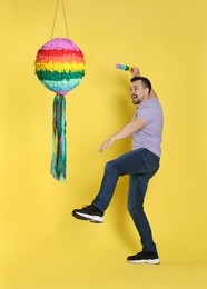 Photo of Emotional man hitting colorful pinata with stick on yellow background