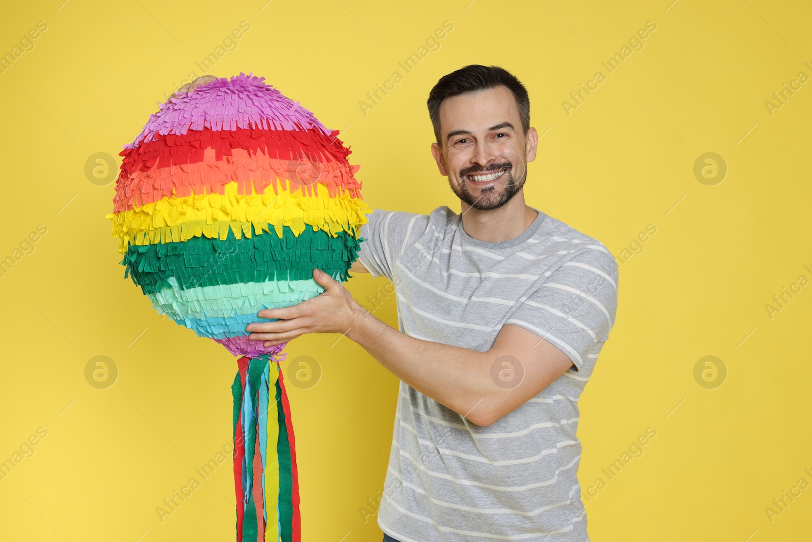 Photo of Happy man with colorful pinata on yellow background