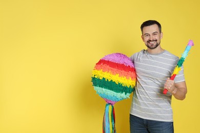 Photo of Happy man with colorful pinata and stick on yellow background, space for text