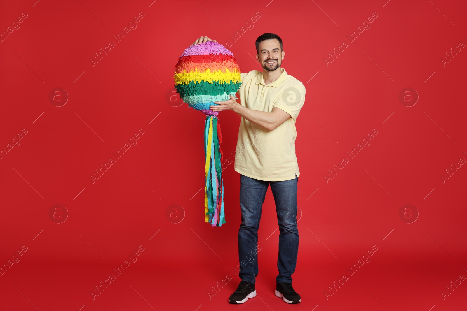 Photo of Happy man with colorful pinata on red background