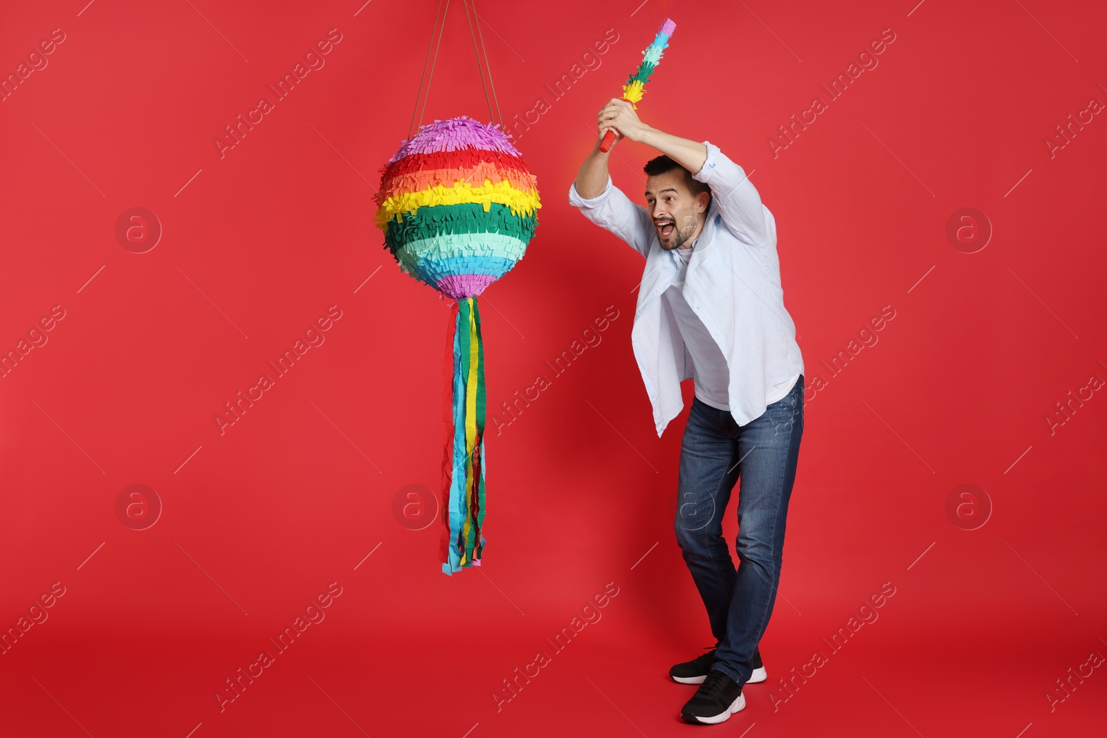 Photo of Emotional man hitting colorful pinata with stick on red background