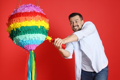 Photo of Happy man hitting colorful pinata with stick on red background