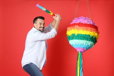 Happy man hitting colorful pinata with stick on red background