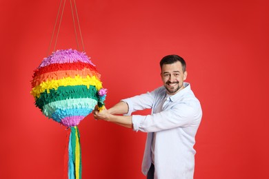 Emotional man hitting colorful pinata with stick on red background