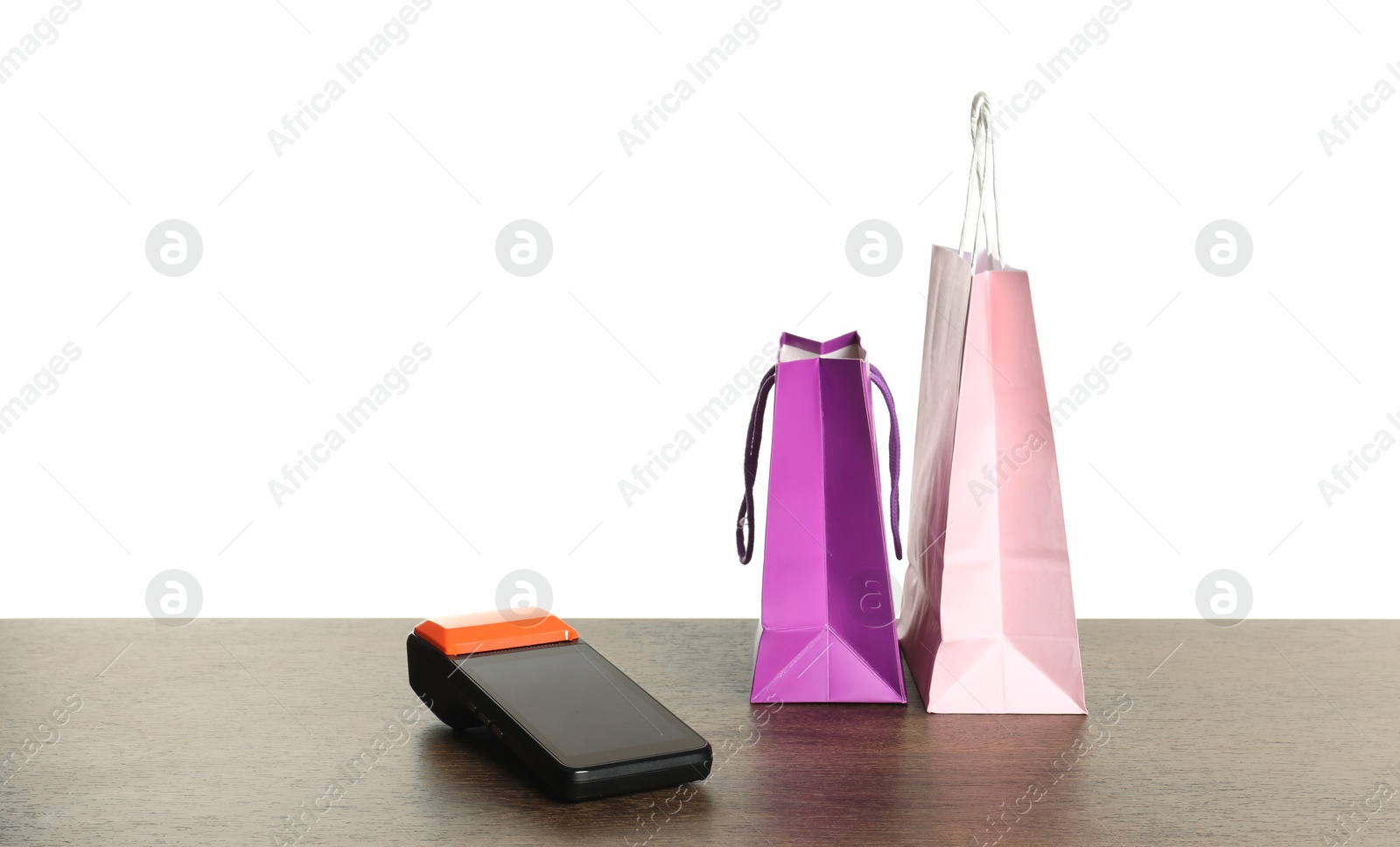 Photo of Payment terminal and shopping bags on wooden table against white background