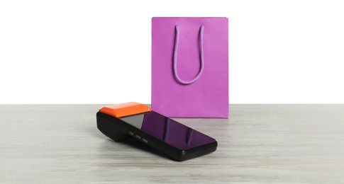 Photo of Payment terminal and shopping bag on wooden table against white background