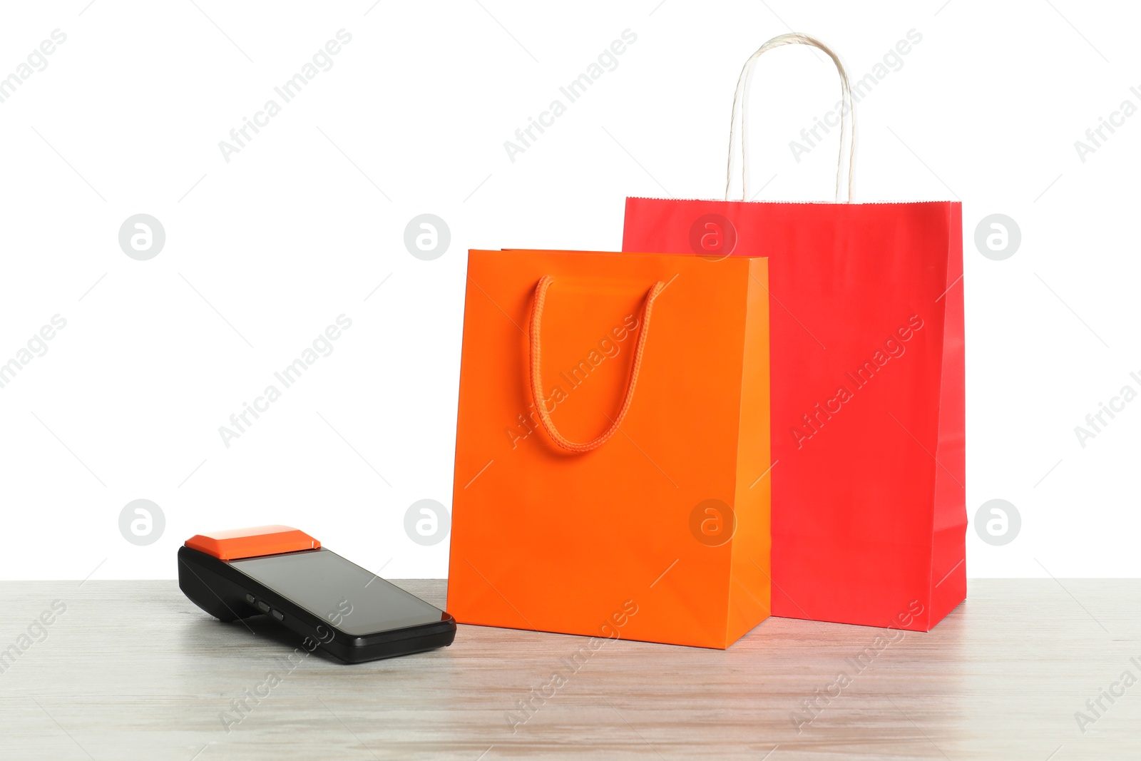 Photo of Payment terminal and shopping bags on wooden table against white background