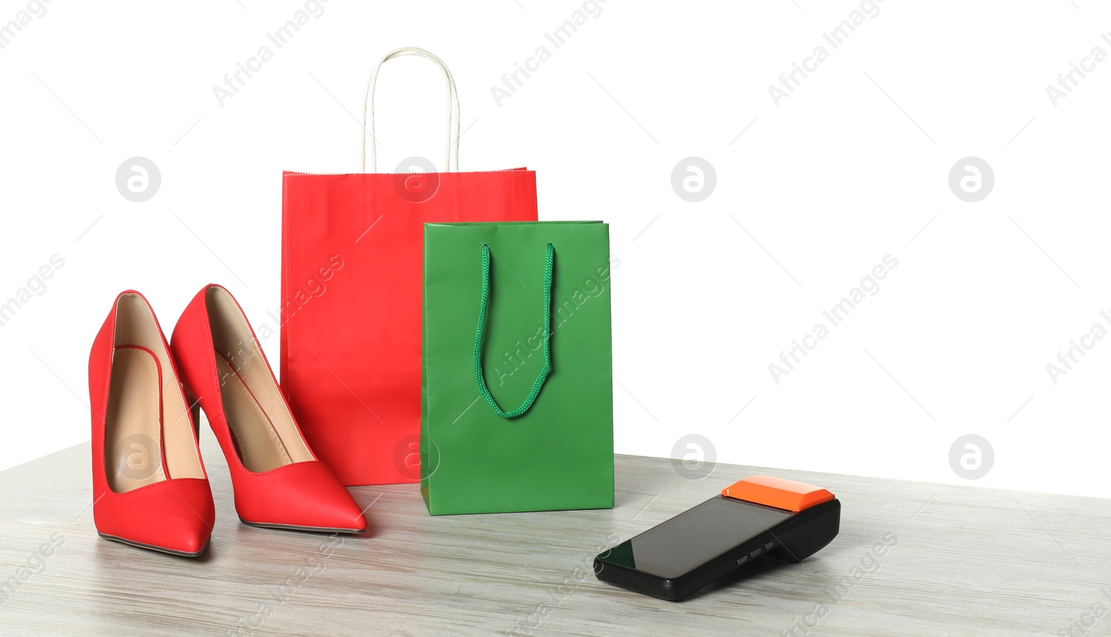 Photo of Payment terminal, shopping bags and high heeled shoes on wooden table against white background