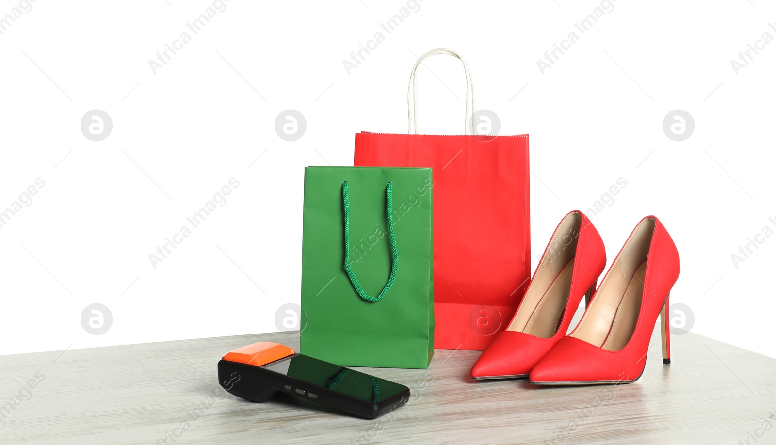 Photo of Payment terminal, shopping bags and high heeled shoes on wooden table against white background