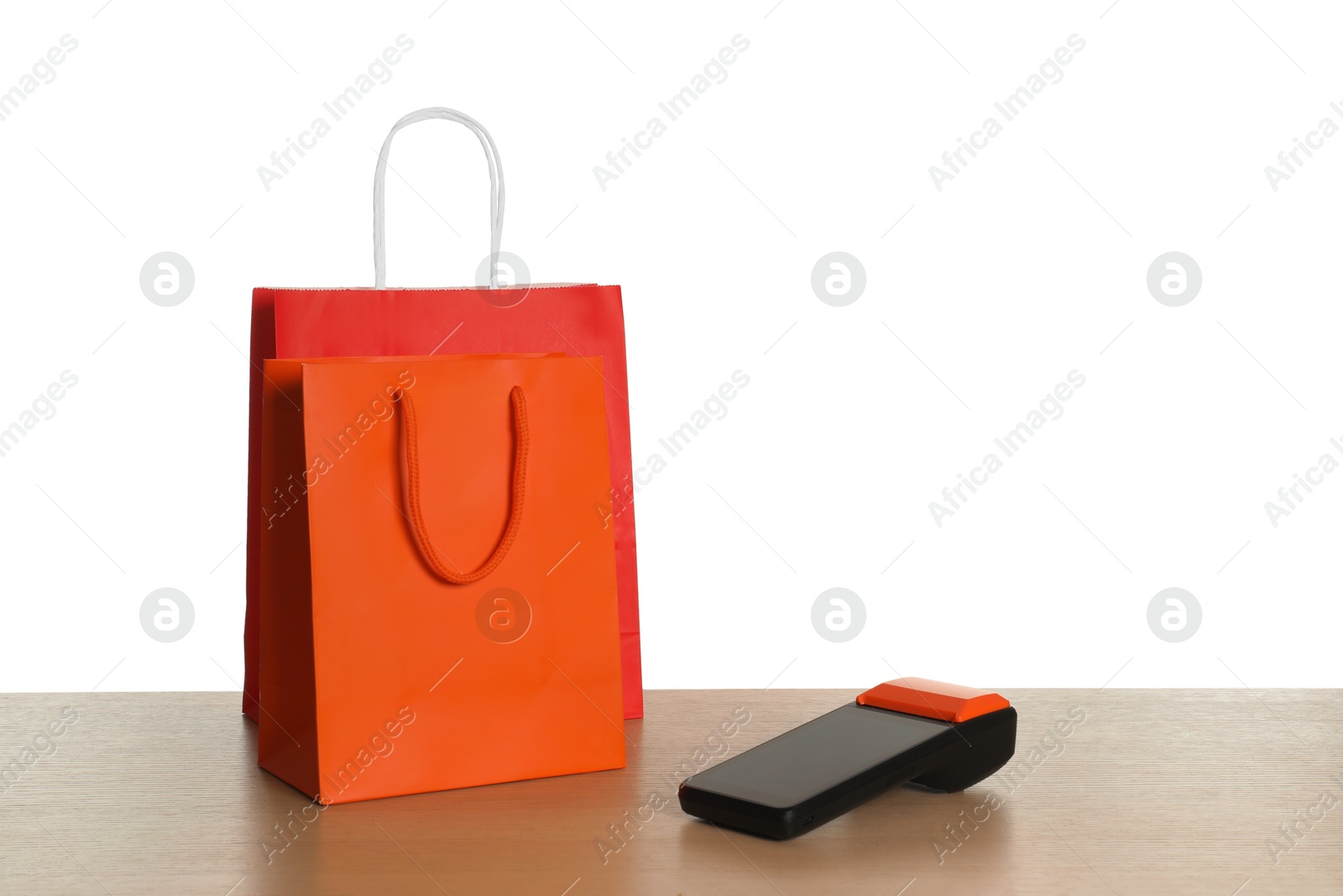 Photo of Payment terminal and shopping bags on wooden table against white background