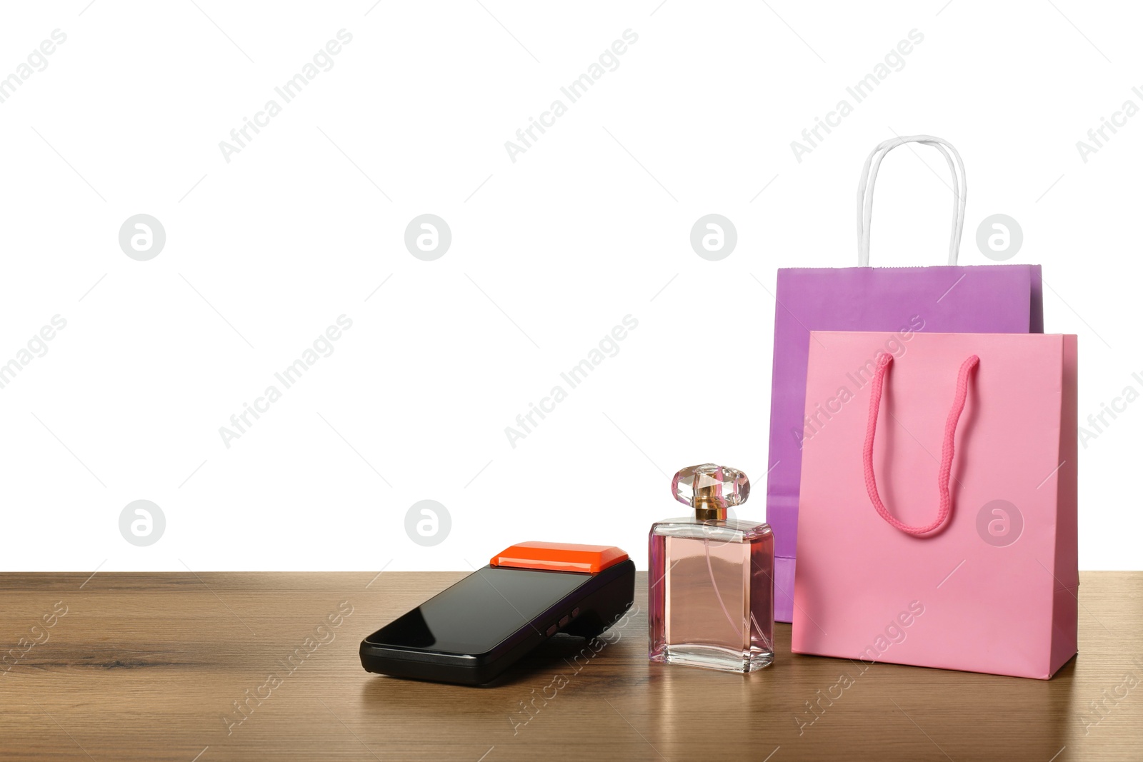 Photo of Payment terminal, perfume and shopping bags on wooden table against white background