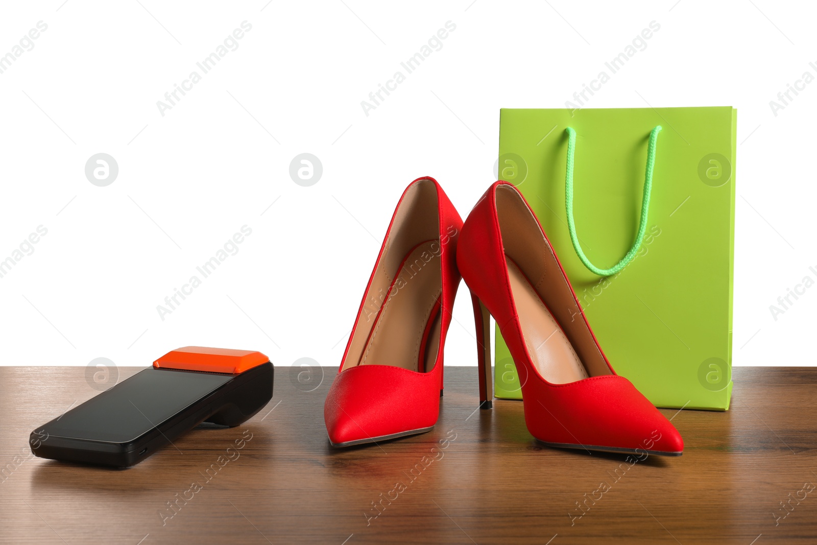 Photo of Payment terminal, shopping bag and high heeled shoes on wooden table against white background