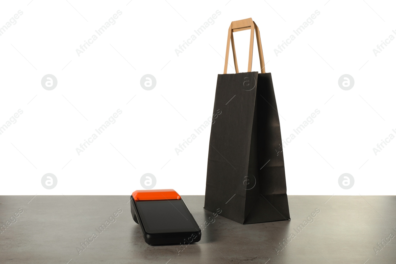 Photo of Payment terminal and shopping bag on grey table against white background