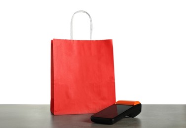 Photo of Payment terminal and shopping bag on grey table against white background