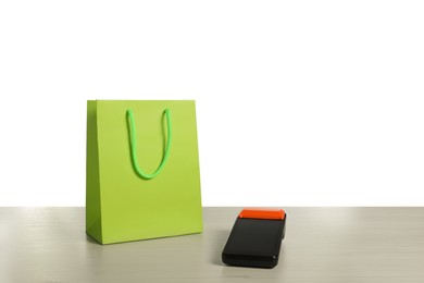 Photo of Payment terminal and shopping bag on wooden table against white background