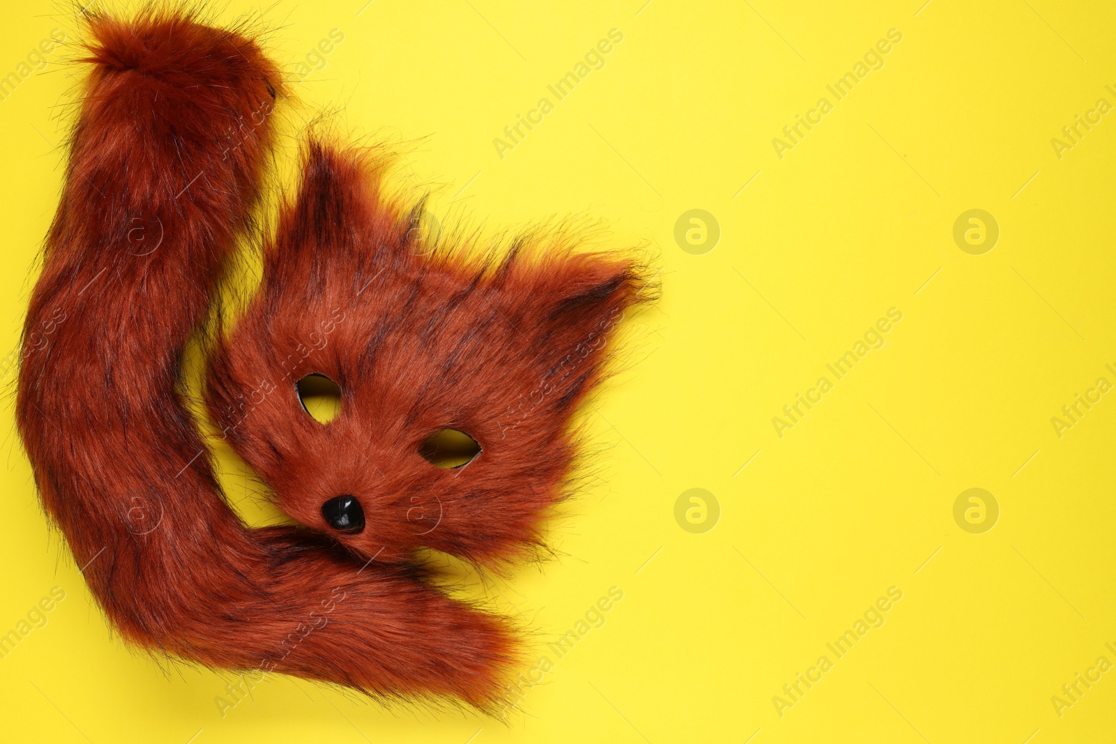 Photo of Quadrobics. Fox mask and tail on yellow background, top view. Space for text