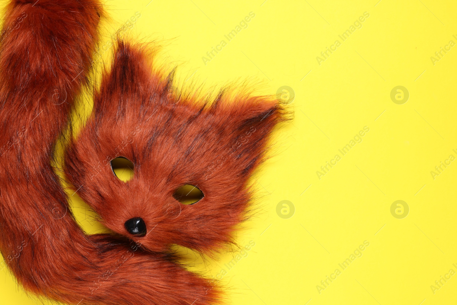 Photo of Quadrobics. Fox mask and tail on yellow background, top view. Space for text