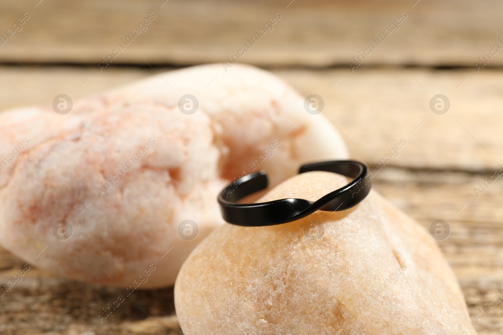 Photo of Stylish black ring and stones on wooden table, closeup