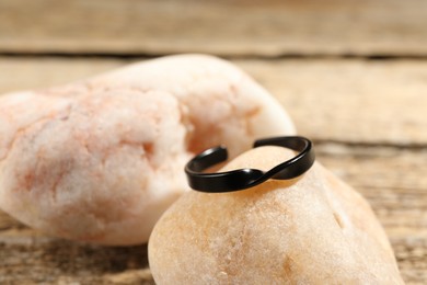 Photo of Stylish black ring and stones on wooden table, closeup