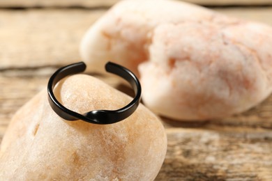 Photo of Stylish black ring and stones on wooden table, closeup