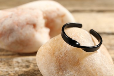 Photo of Stylish black ring and stones on wooden table, closeup