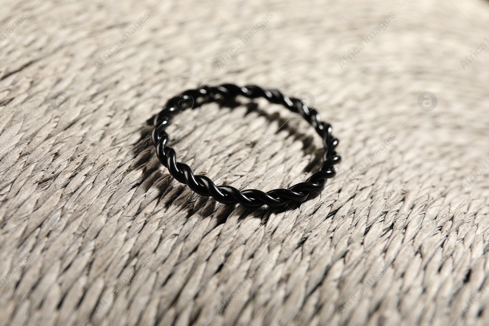 Photo of Stylish black ring on wicker surface, closeup