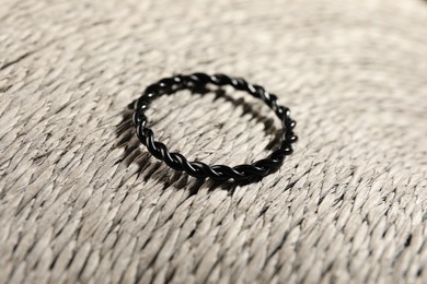 Photo of Stylish black ring on wicker surface, closeup