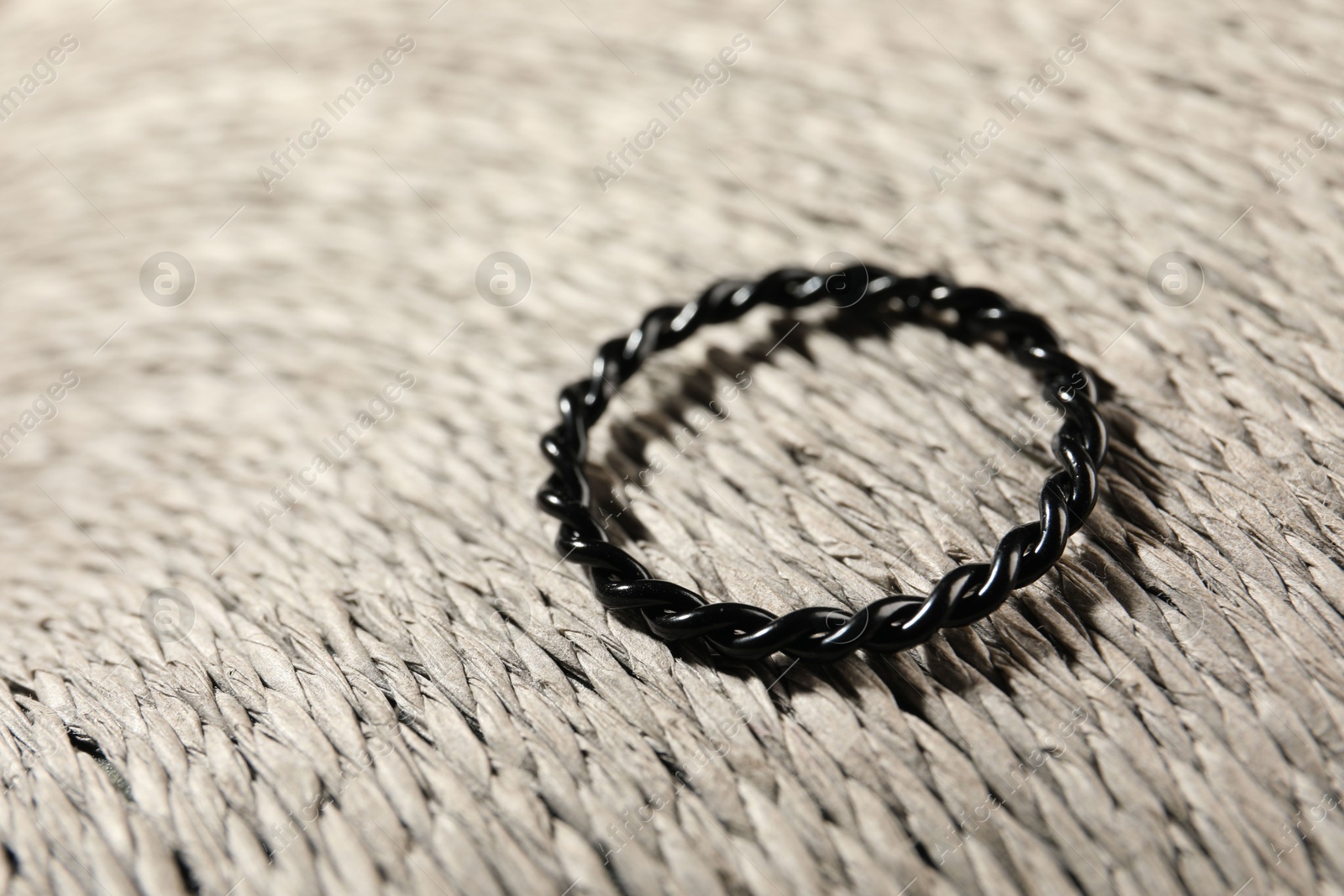 Photo of Stylish black ring on wicker surface, closeup. Space for text