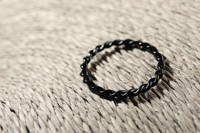 Stylish black ring on wicker surface, closeup. Space for text