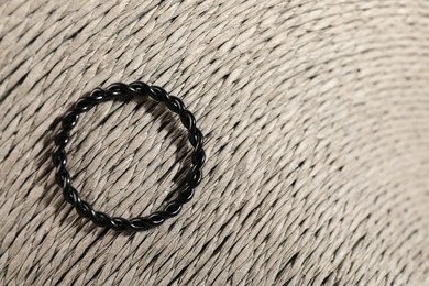 Photo of Stylish black ring on wicker surface, top view. Space for text