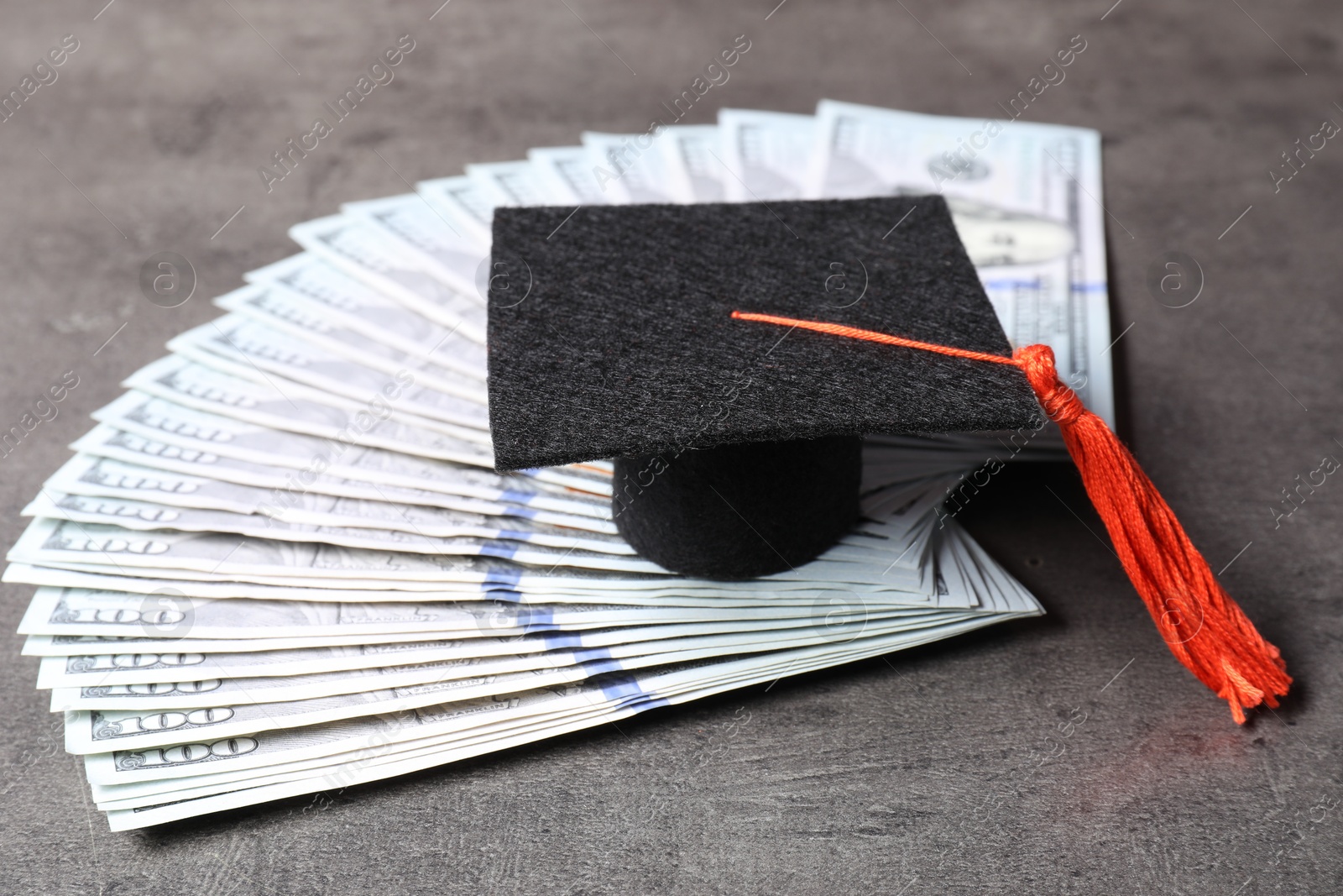 Photo of Graduate hat and dollar banknotes on grey table, closeup. Tuition payment