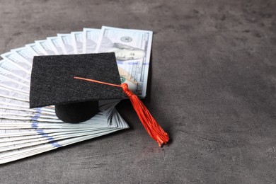 Photo of Tuition payment. Graduate hat and dollar banknotes on grey table, closeup. Space for text