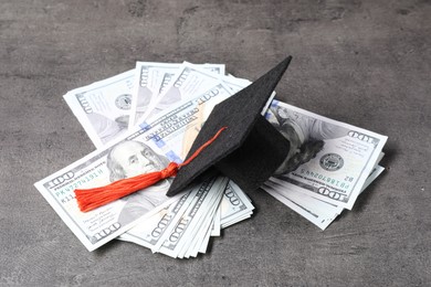 Photo of Graduate hat and dollar banknotes on grey table, closeup. Tuition payment