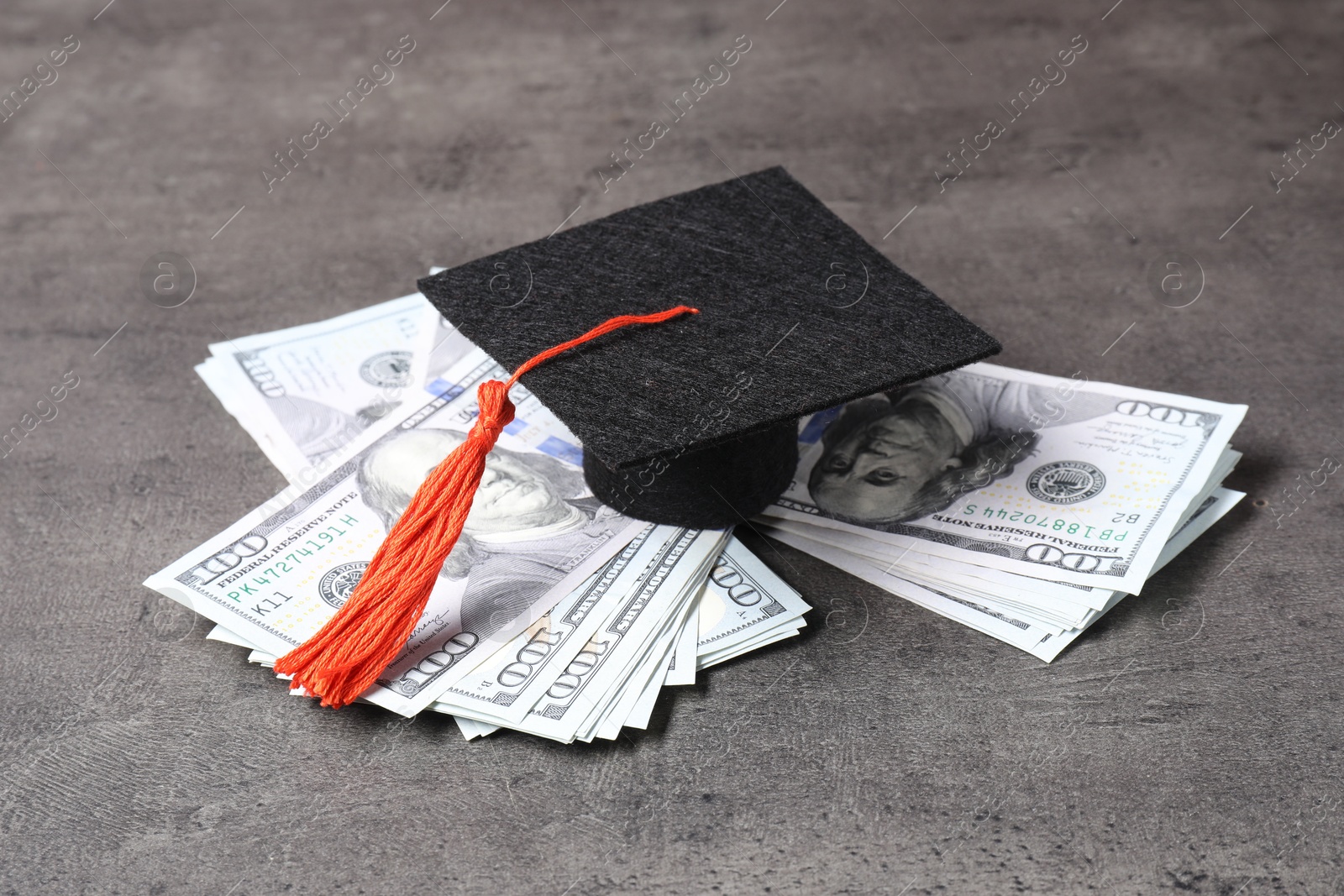 Photo of Graduate hat and dollar banknotes on grey table, closeup. Tuition payment