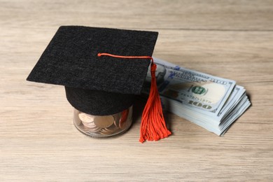 Photo of Graduate hat, dollar banknotes and coins on wooden table, closeup. Tuition payment