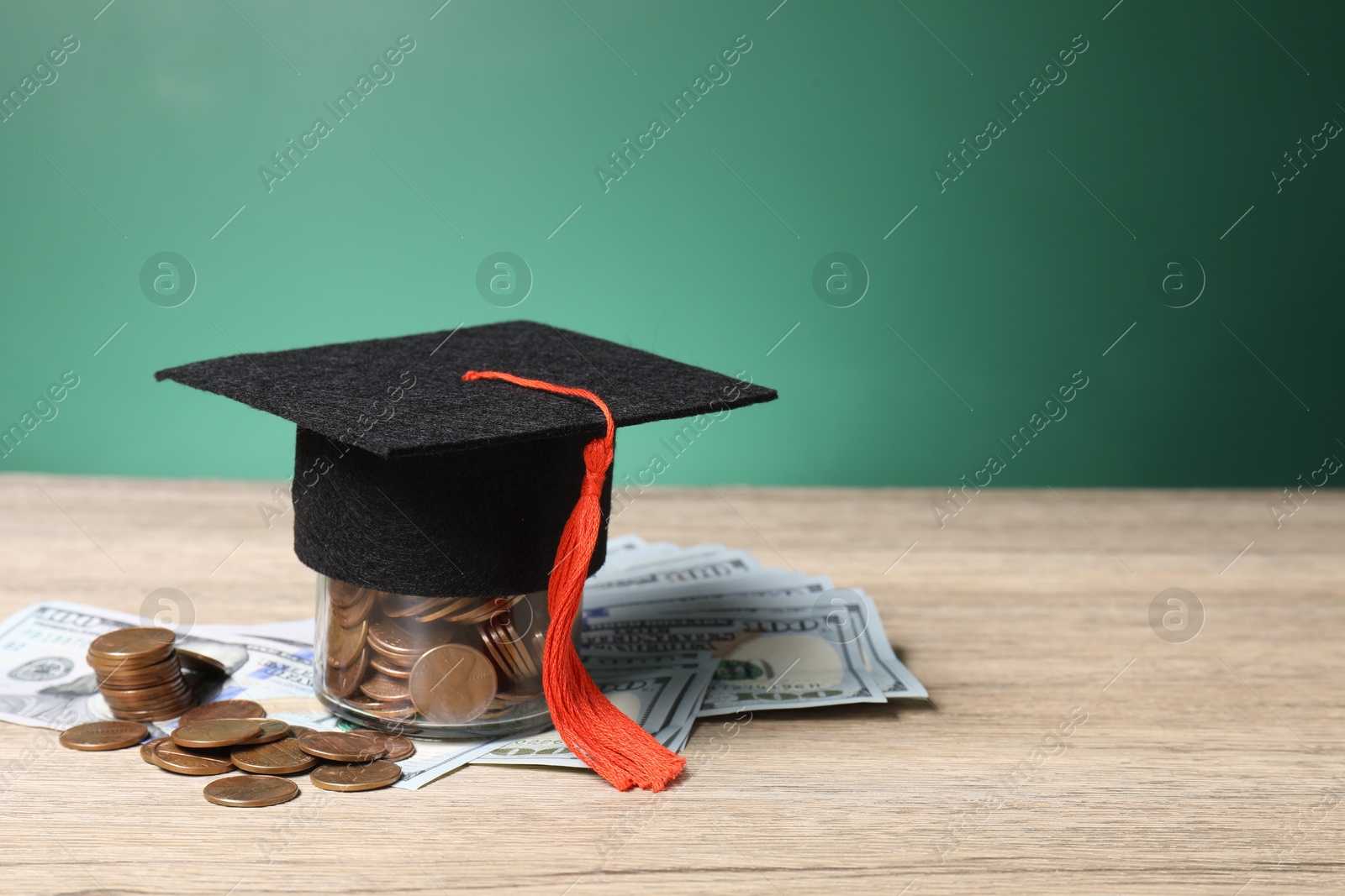 Photo of Tuition payment. Graduate hat, dollar banknotes and coins on wooden table, closeup. Space for text